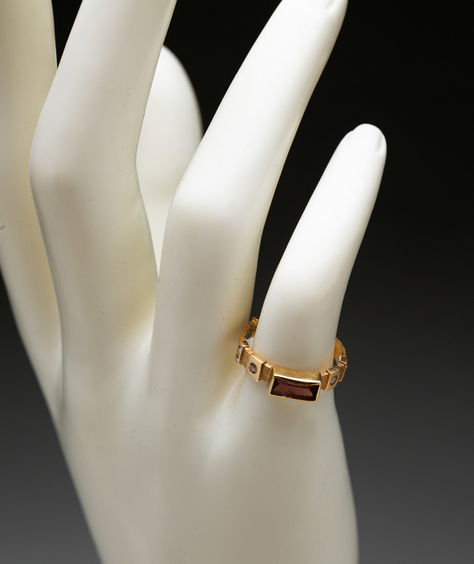 18K GOLD AND AMETHYST RING, DOUGLAS ZARUBA.: American, late 20th Century. Stamped '750 ZAR UBA' (Douglas Zaruba, American jeweler), brushed yellow gold slender band with center fancy cut amethyst, ten small round diamonds recess set around band.