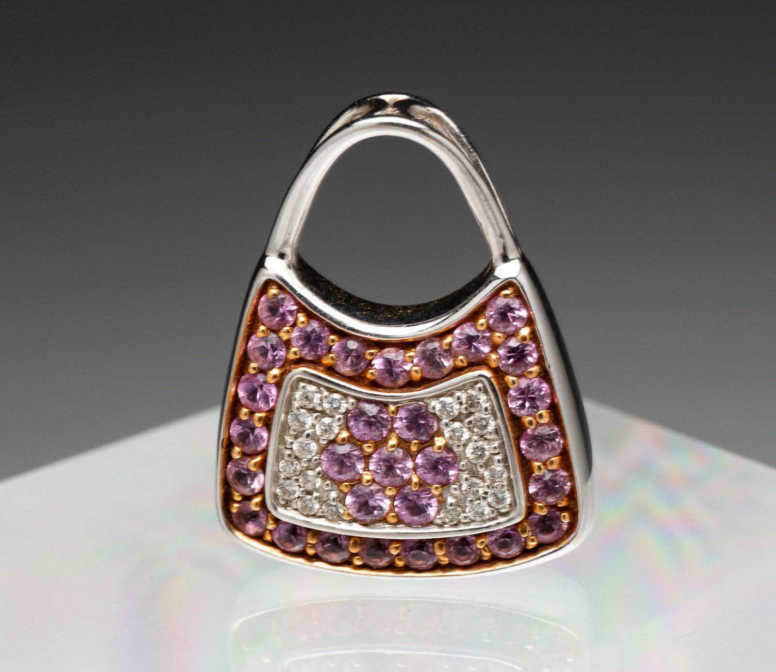18K MIRABELLE DIAMOND & SAPPHIRE PURSE PENDANT.: Late 20th Century. 18K white gold purse pendant pave set with round diamonds and pink sapphires. Approx. .87"l. .62"w., 6gr. Marked with M hallmark, diamond mark, and "18k".