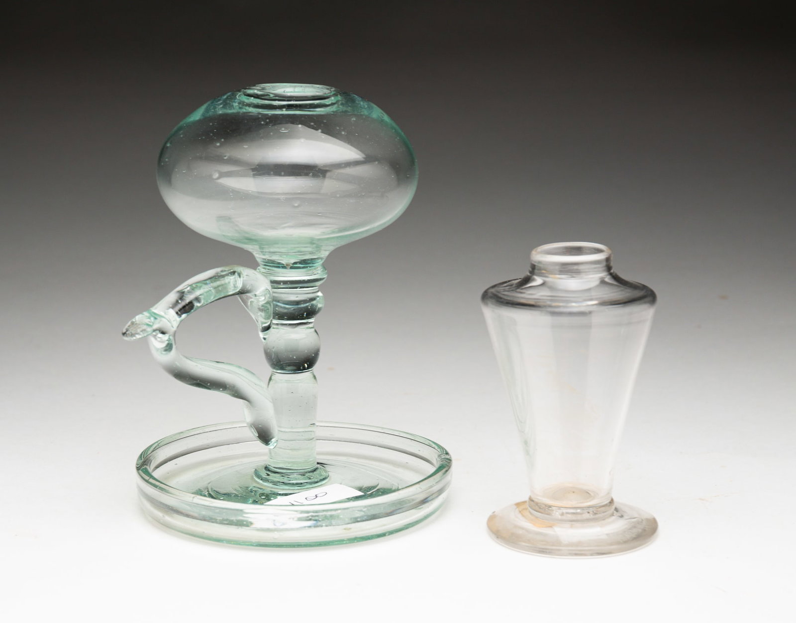 TWO WHALE OIL LAMPS.: TWO WHALE OIL LAMPS. American, second quarter 19th Century. Flint glass. One has a slightly aqua tint, elliptical font, applied handle and saucer base, 5"h. and the other is a footed sparking lamp, 3.