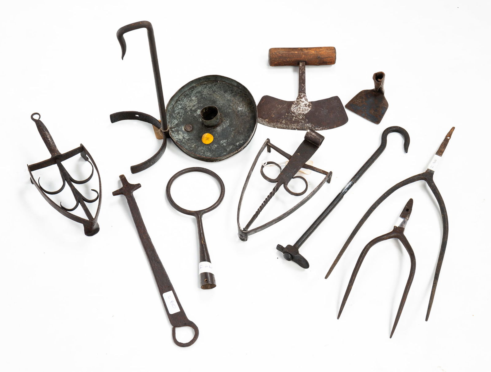 GROUP OF FORGED IRON ITEMS.: GROUP OF FORGED IRON ITEMS. American, first half 19th Century. Two sad iron trivets, stove lid lifter, pastry board scraper, hearth hook, meat forks, hanging candle with tin pan,12.5"h., chopper, spli