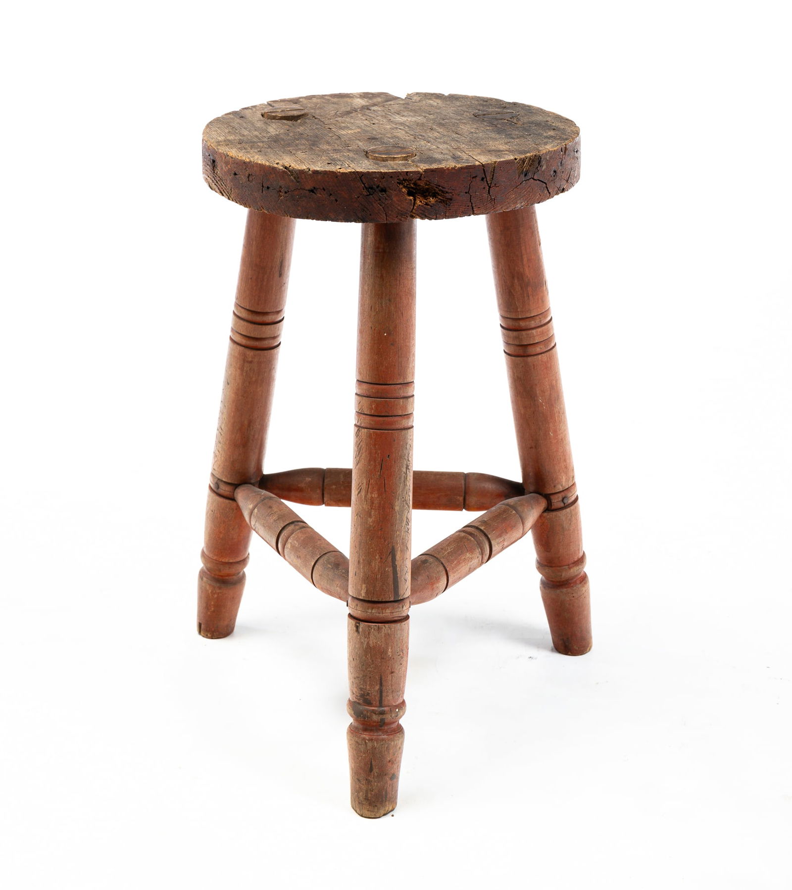 THREE LEG MILKING STOOL.: THREE LEG MILKING STOOL. American, second quarter 19th Century. Round wormy chestnut seat and turned maple legs and stretcher with worn red wash. Some wear and loss. 21"h. 12.75" dia.