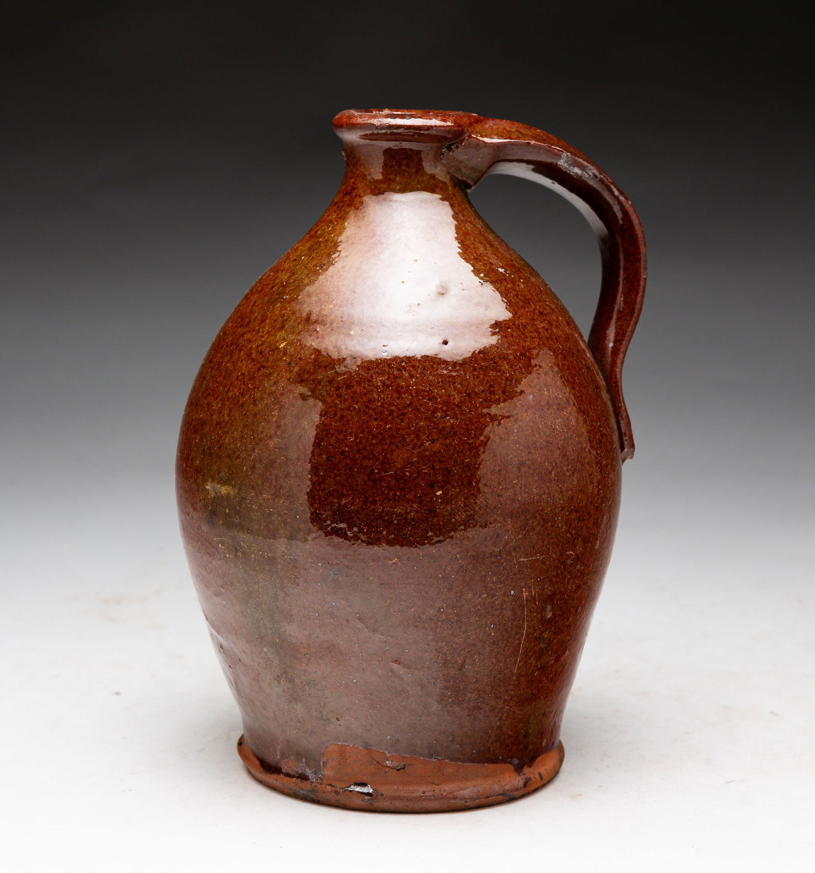 REDWARE SMALL JUG.: American (New England), mid-19th Century. Glazed small jug with applied pulled handle. Surface wear. 7.5"h.