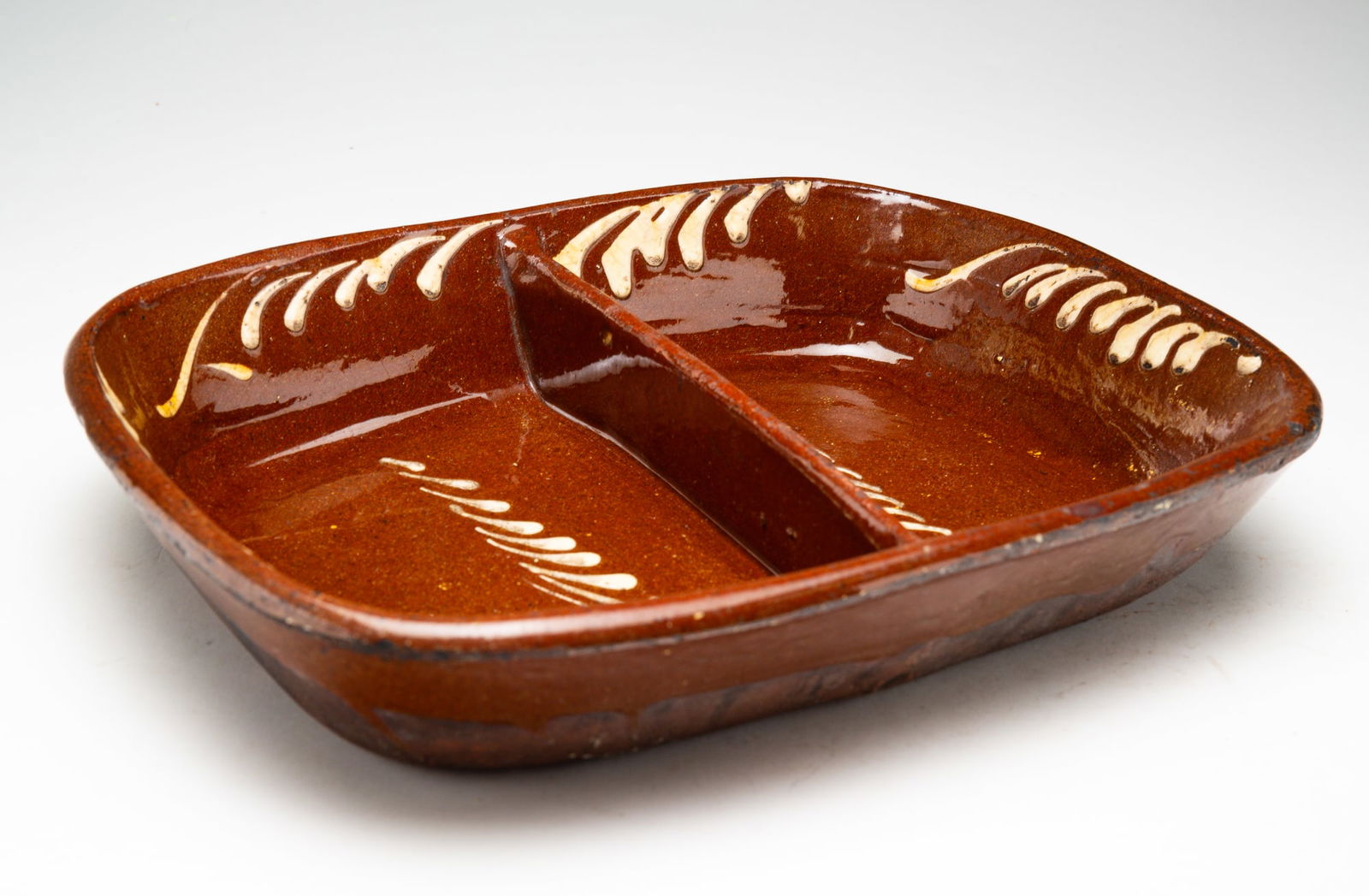 REDWARE DIVIDED DISH.: American, mid-19th Century. Rectangular dish with central divider. High glaze in brown with white feather drips. Edge wear. 2.75"h. 14"w. 11.5"d.