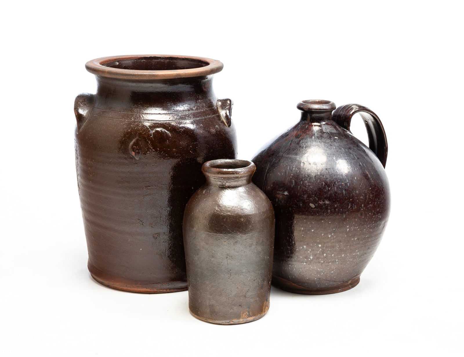 THREE GLAZED REDWARE VESSELS.: American, second half 19th Century. Three pieces in high brown glaze. Small jar, surface wear and chips, 7.75"h. Jug with applied strap handle, crack to bottom, 10"h. Double handled crock with incised