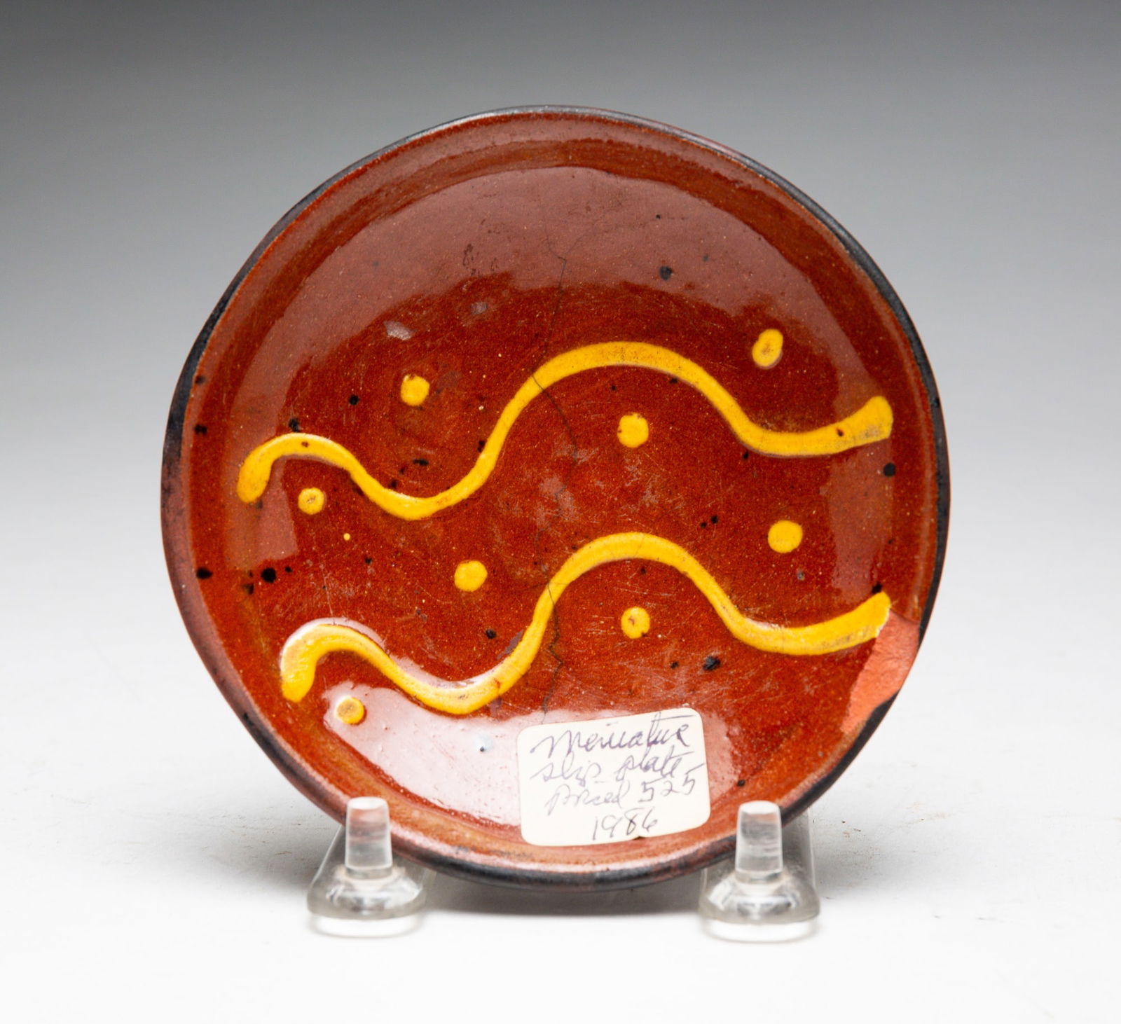 MINIATURE REDWARE PLATE.: American, mid-19th Century. Small round plate with free hand slip decoration. Chip to rim and hairline. 4.25" dia.Provenance: The Collection of the late Dr. Compton, Tipton, IN.