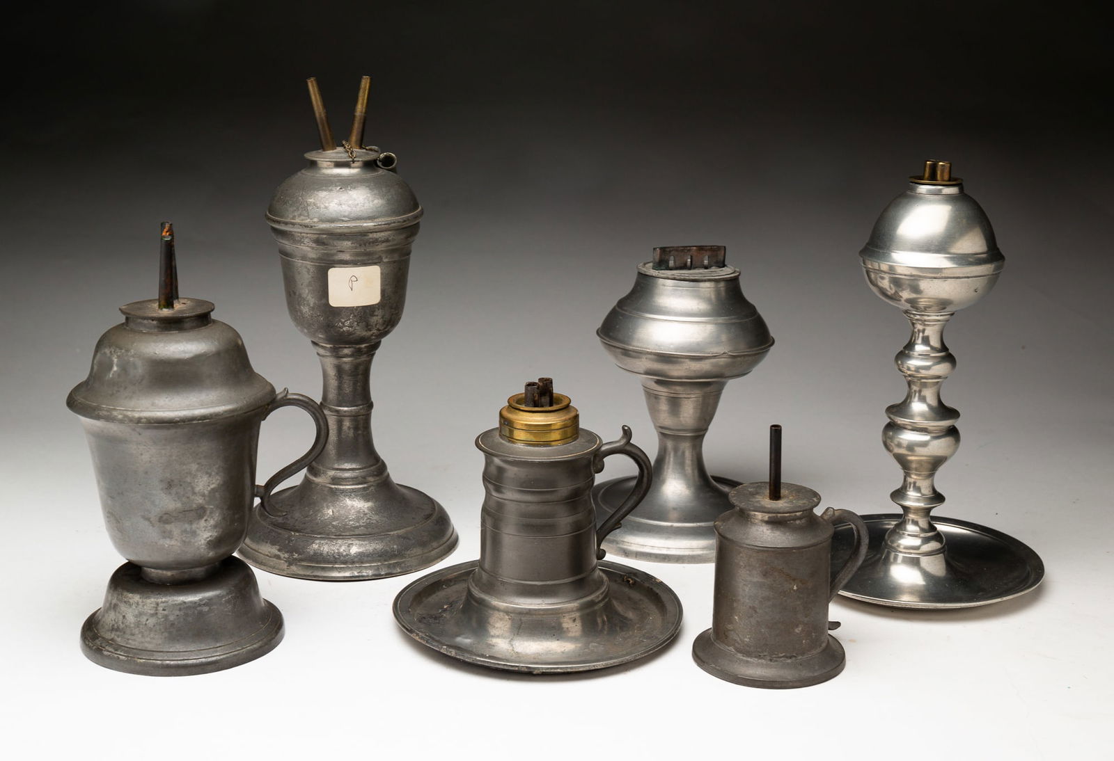 SIX PEWTER LAMPS.: American, mid-19th Century. Double burner whale oil, baluster stem and saucer base, 8.25"h. inverted acorn font, camphene burner and plain stem, 9.5"h., wide single wick burner and plane stem, 5.75"h.