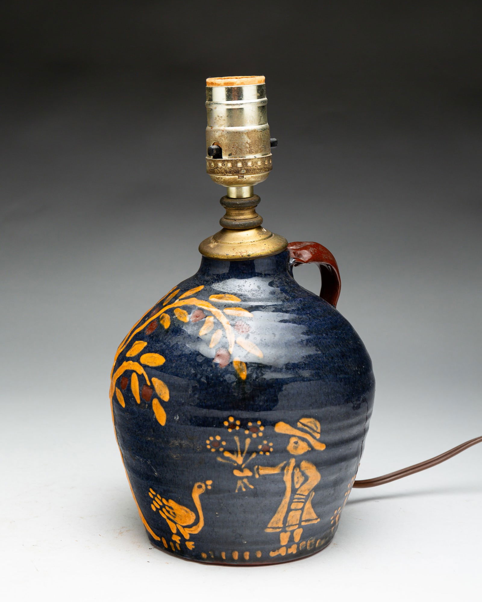 TURTLE CREEK POTTERY REDWARE LAMP.: American, dated (19)85. Signed Cathy Gatch. Blue field with painted decoration and brown applied strap handle. 6.5"h. plus lamp parts. Glaze wear.