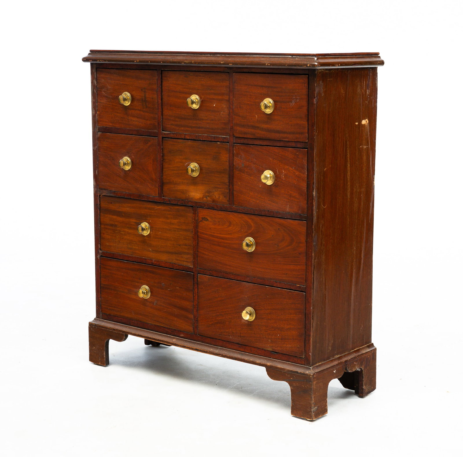 TEN-DRAWER APOTHECARY.: American, mid-19th Century. Mahogany and mahogany veneer, molded top, hand-dovetailed drawers, brass knobs, bracket base. Wear. 29"h. 25.75"w. 9.5"d.