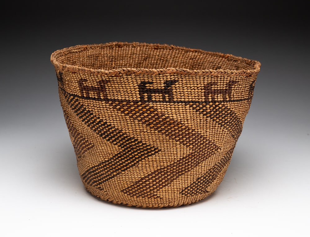 SKOKOMISH TWINED BASKET.: Circa 1890-1920. Brown and black zigzags with ten dogs on the border. Very good condition. 7"h. 11"dia.We do not guarantee tribal attributions for American Indian / First Nations items.