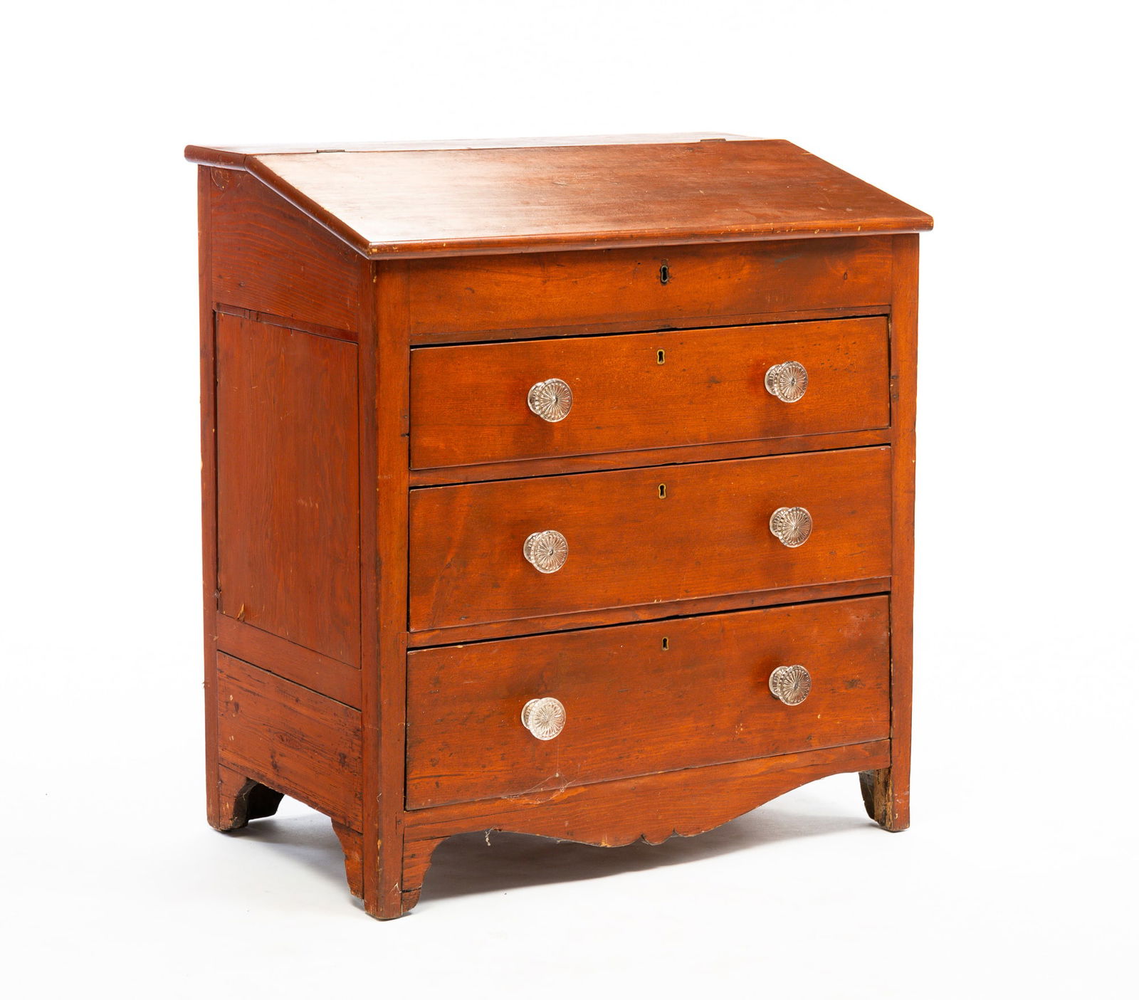 SLANT-LID DESK.: American, mid-19th Century. Hinged lid, three dovetailed drawers with period glass pulls, shaped apron and fitted interior. Wear along edges, refinished with traces of original red. 36.75"h. 32.875"w.