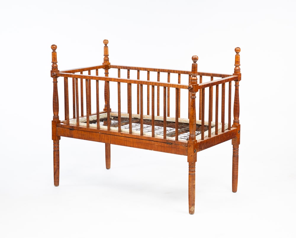 SHERATON BABY CRIB.: American, second quarter 19th Century. Tiger maple. Thin turned corner posts with spherical finials, round spindles, wire springs and one side is hinged. Old dry finish. 42.5"h. 25.5"w. 48.5"l.