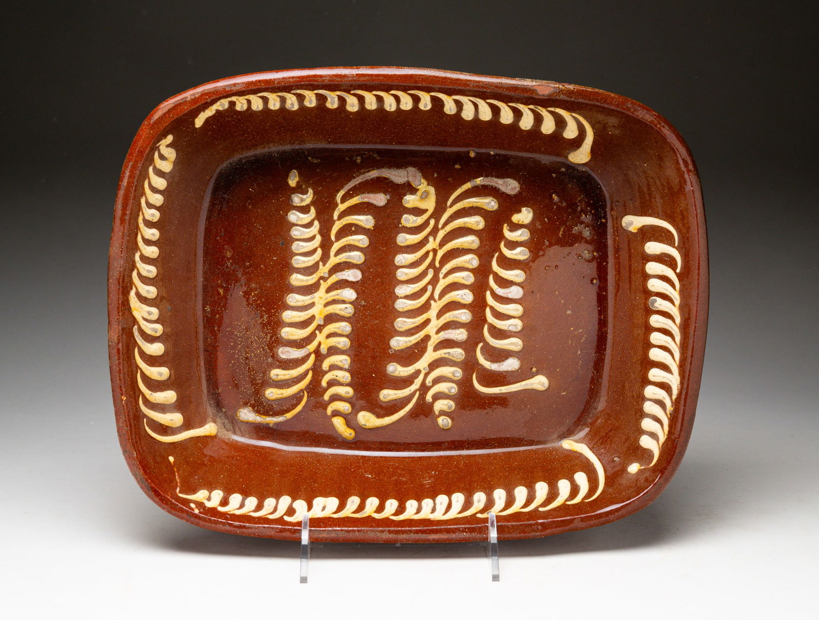 REDWARE LOAF PAN WITH SLIP DECORATION.: American, mid-19th Century. Canted sides, rounded corners and plume like pattern. Wear and glaze flaking. 2.75"h. 15.25"w.