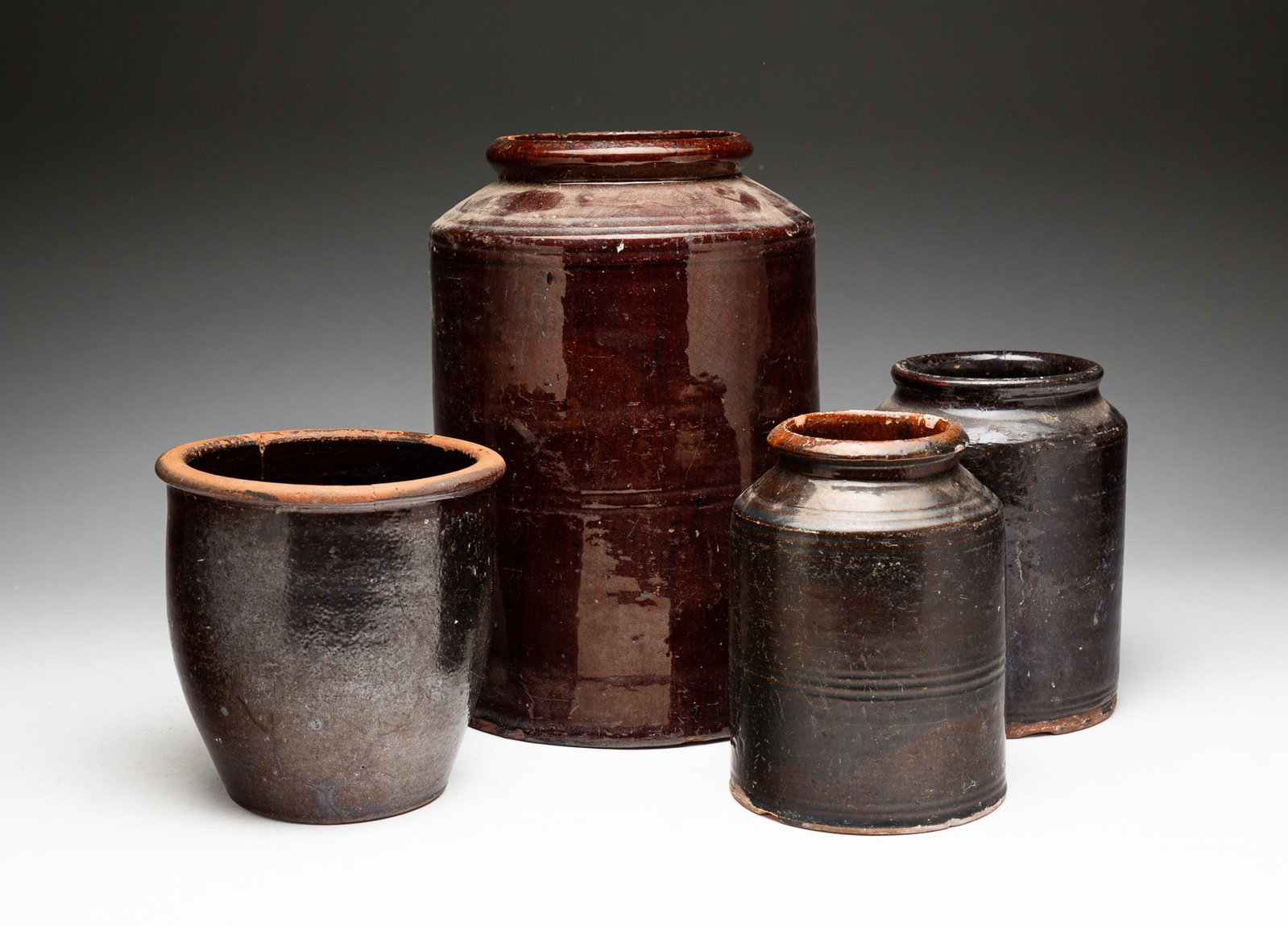 FOUR REDWARE JARS.: American, mid-19th Century. All four have dark brown glaze. Three have straight sides, sloped shoulders and rolled lips. 11"h., 6.75"h. And 6.25"h. An ovoid jar with rolled lip. 5.75"h. Chips, wear an