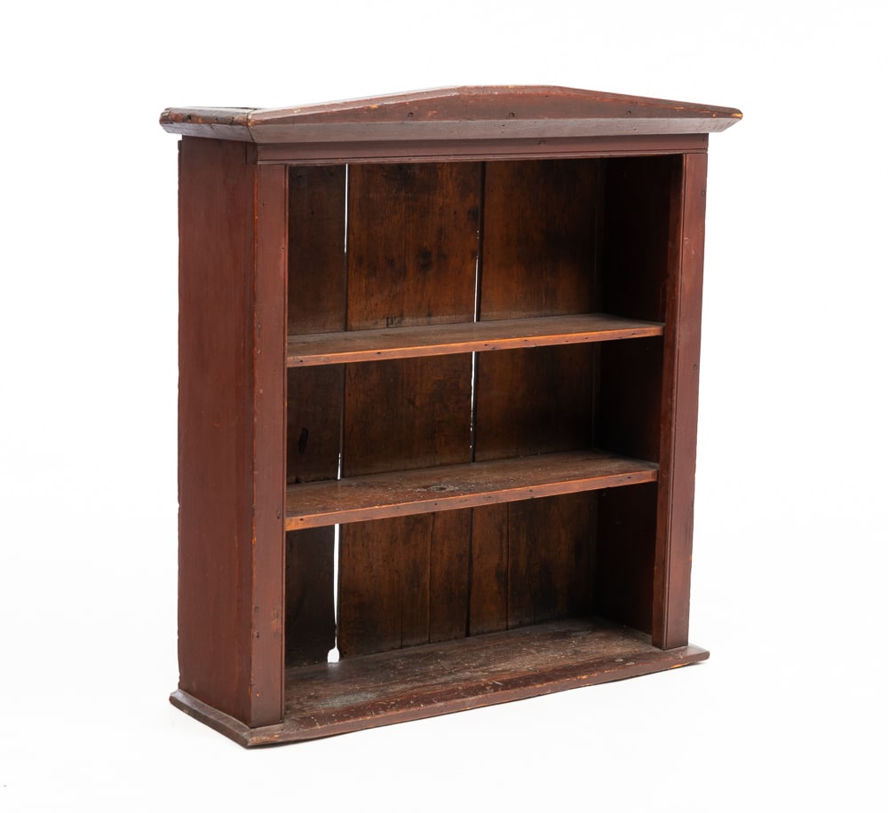 PAINTED SET OF SHELVES.: American, mid-19th Century. Poplar. Low peaked cornice, opening with beaded edge, three shelves and worn original red wash. Some wear, shrinkage and age loss. 33"h. 31"w. 10"d.