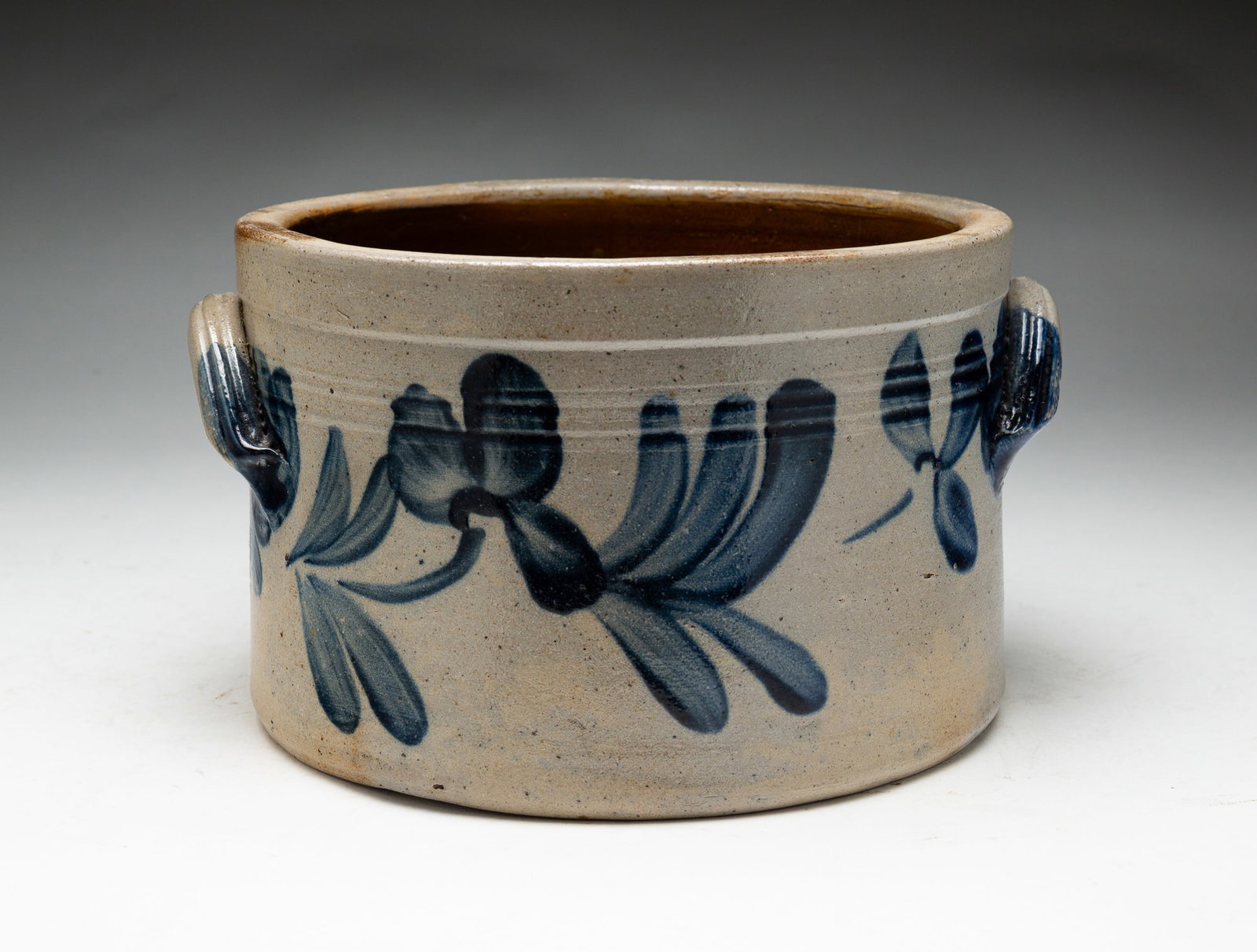 DECORATED STONEWARE CROCK.: American, second half 19th Century. Double handled crock with flower and leaf decoration and grooved banding. Chips, surface wear and crack. 5.25"h.