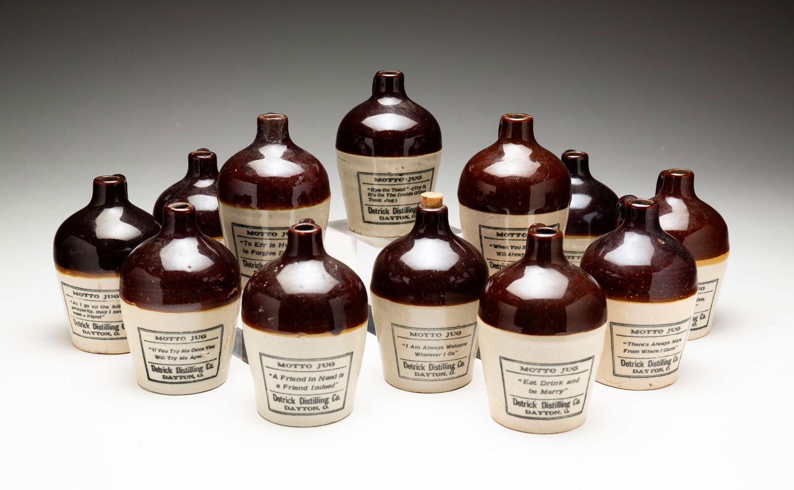 SET OF 12 DETRICK WHISKEY STONEWARE MINIATURE MOTTO JUGS.: American, early-20th Century. Detrick Distilling Company, Dayton, Ohio. These jugs are the version with the border around the motto. Base chip on "If you try me...". Small chips to base and chip to sp