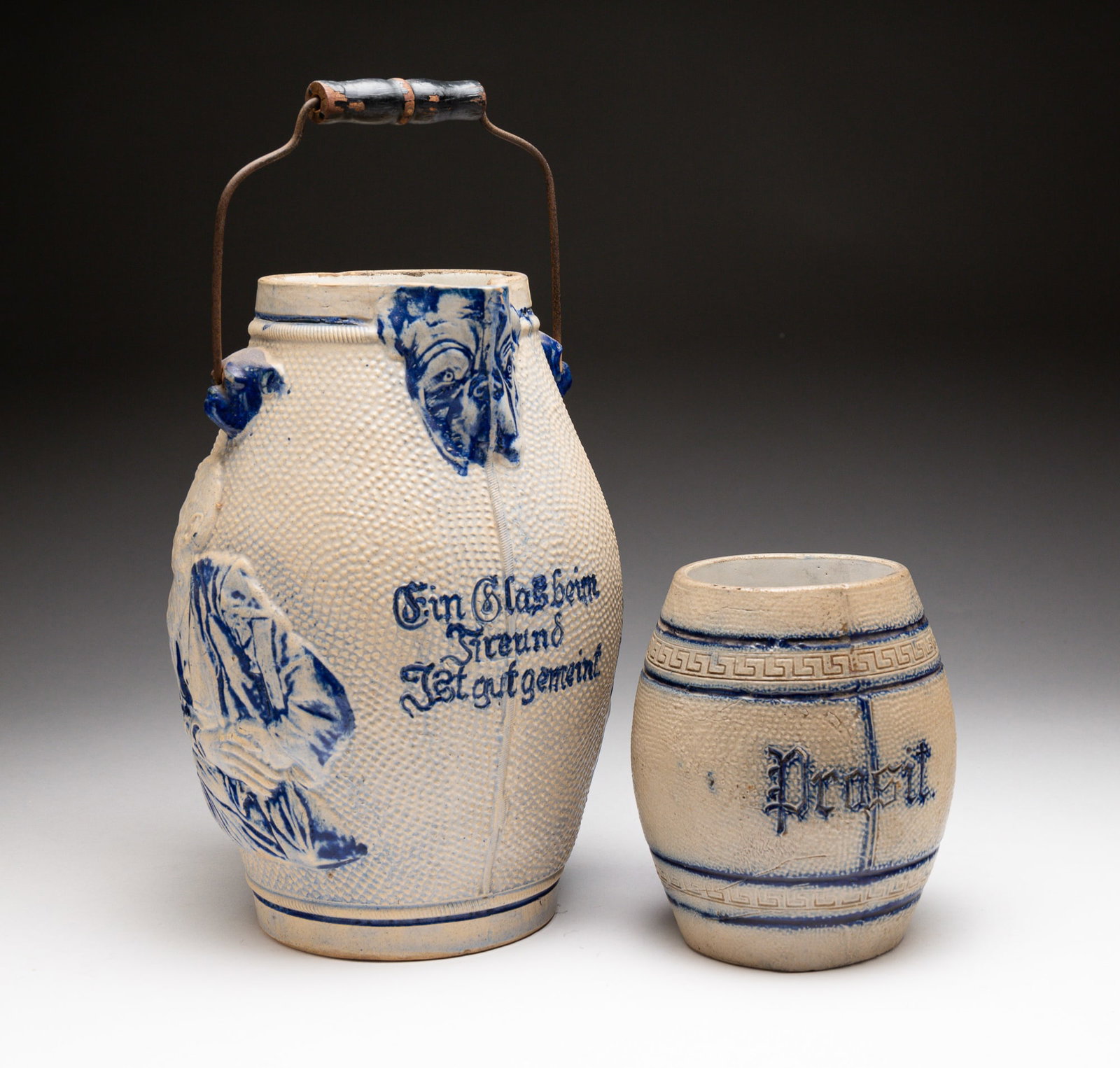 BLUE AND GRAY SALT-GLAZED STONEWARE PITCHER AND STEIN.: American, late-19th Century. Attributed to Whites Pottery, Utica, NY. Pitcher molded with portraits of men and embossed "Ein Glas beim Freund Ist gut gemeint" ("A glass with a friend is well-intention