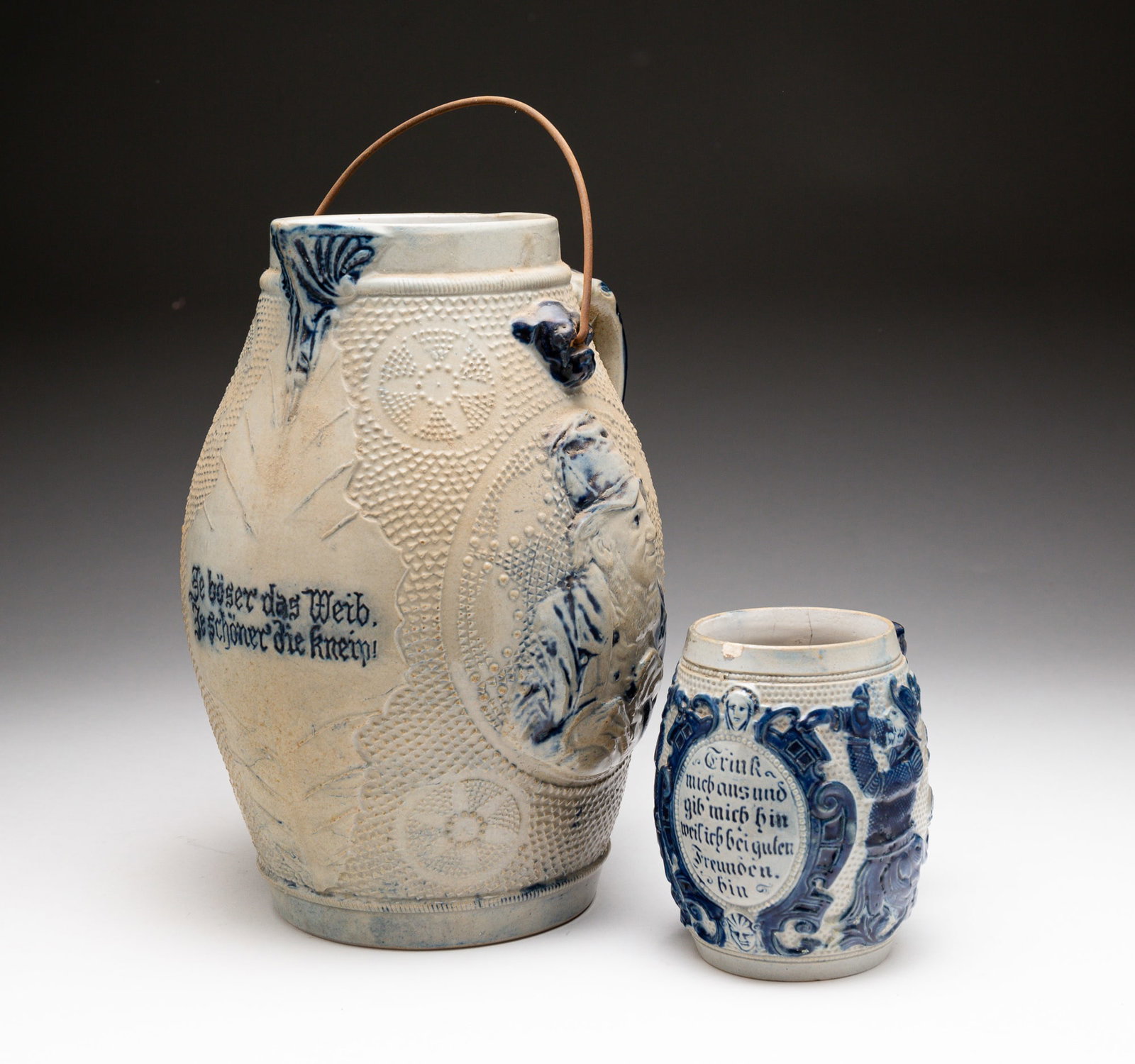 BLUE AND GRAY SALT-GLAZED STONEWARE PITCHER AND STEIN.: American, late-19th Century. Attributed to Whites Pottery, Utica, NY. Pitcher molded with portraits of men and embossed with "Je böser das Weib, Je schöner die kneip!" ("The meaner the woman