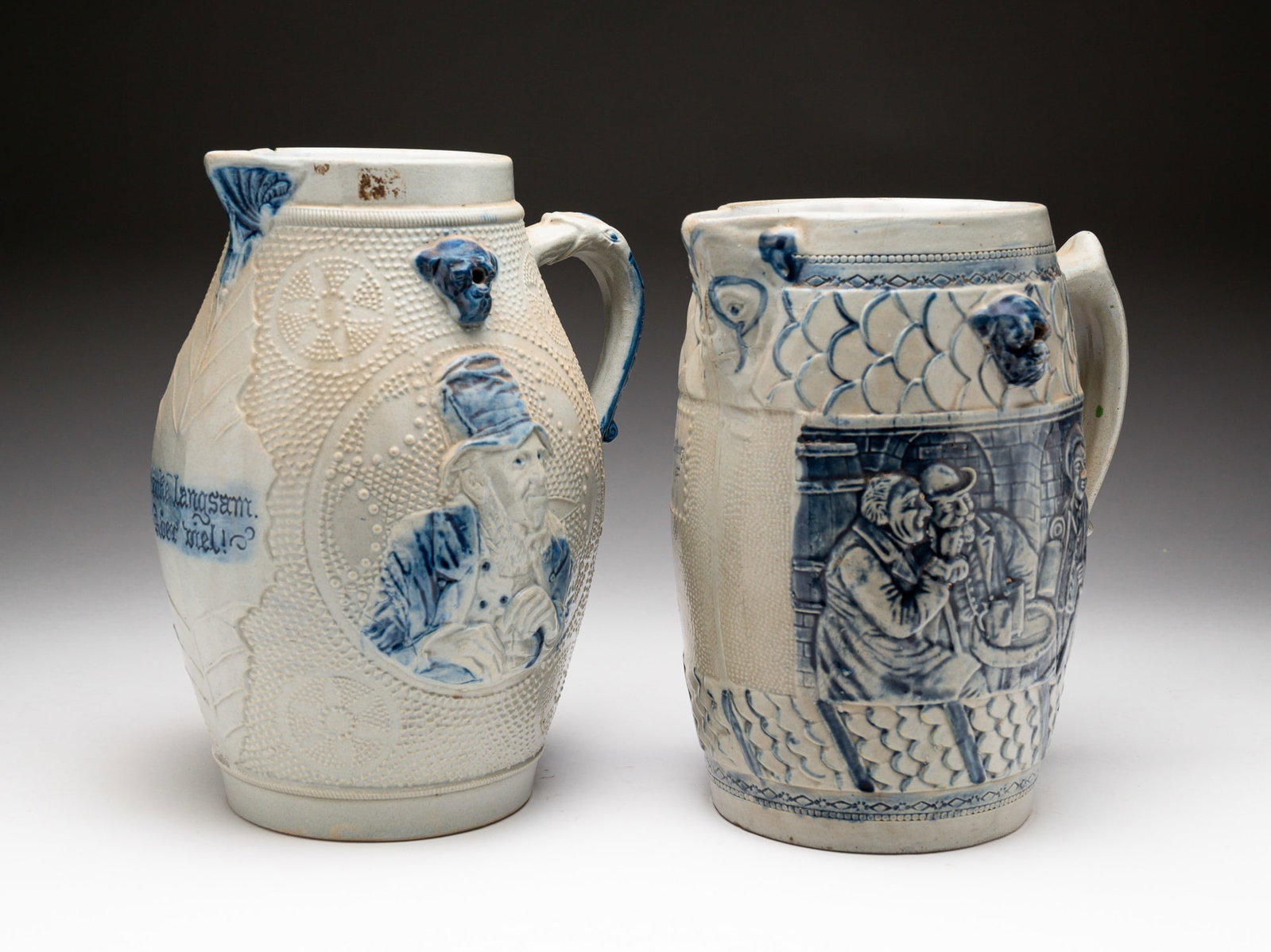 TWO BLUE AND GRAY SALT-GLAZED STONEWARE PITCHERS.: American, late-19th Century. Attributed to Whites Pottery, Utica, NY. First pitcher molded with portraits of men and embossed with "Trinke Langsam. Aber viel!" ("Drink slowly. But a lot!"). Embossed "