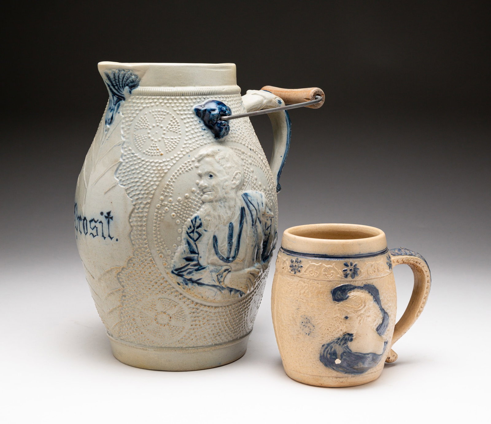 BLUE AND GRAY SALT-GLAZED STONEWARE PITCHER AND STEIN.: American, late-19th Century. Attributed to Whites Pottery, Utica, NY. Pitcher molded with portraits of George Washington and Abraham Lincoln and embossed with "Prosit" (A Latin word from which the Ger