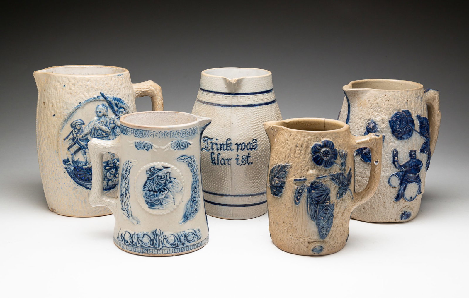 FIVE BLUE AND GRAY SALT-GLAZED STONEWARE PITCHERS.: American, late-19th Century. Attributed to Whites Pottery, Utica, NY. One pitcher molded with a portrait of General von Steuben and a Revolutionary War scene with embossed "6" on underside; another mo