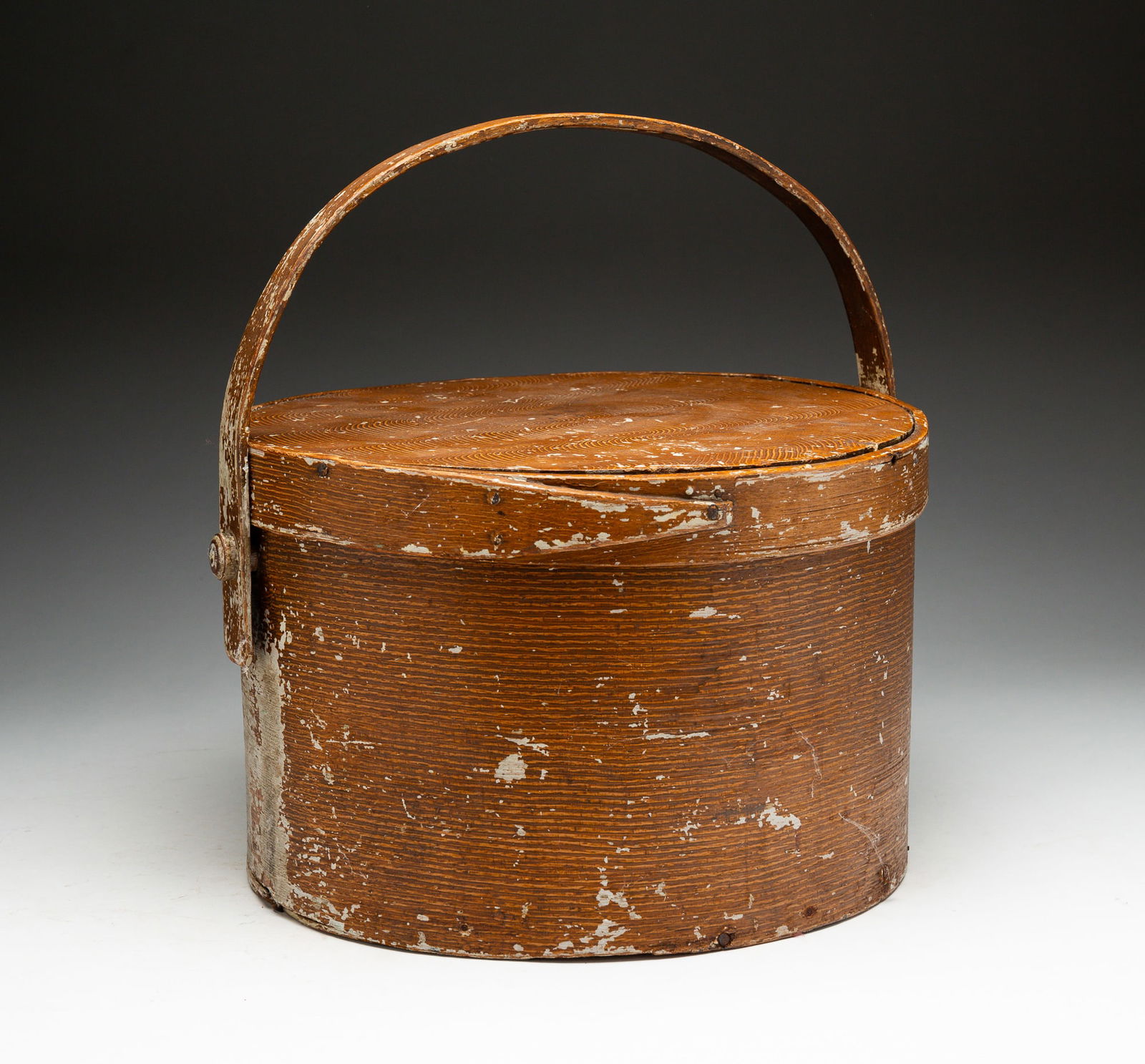 GRAIN PAINTED BENTWOOD CARRY ALL.: American, late-19th Century. Oak and pine. Lid with finger joint, bottom with lap joints. Combed tan graining has wear. Some edge loss. 7.5"h. 11.75"dia.
