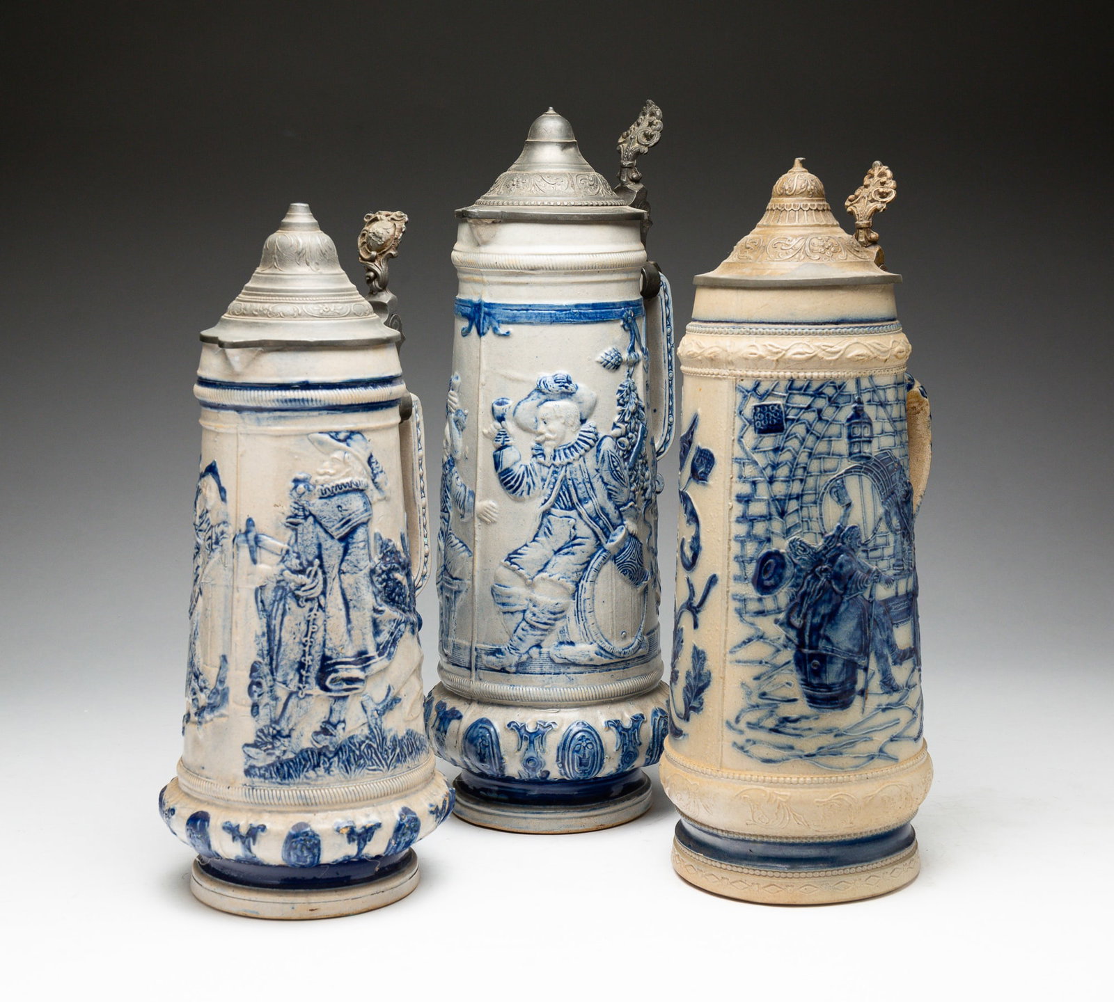 THREE BLUE AND GRAY SALT-GLAZED STONEWARE STEINS.: American, late-19th Century. Attributed to Whites Pottery, Utica, NY. The first molded with tavern scene and embossed with German sayings. With pewter lid. Impressed "8" on underside. With chips and h