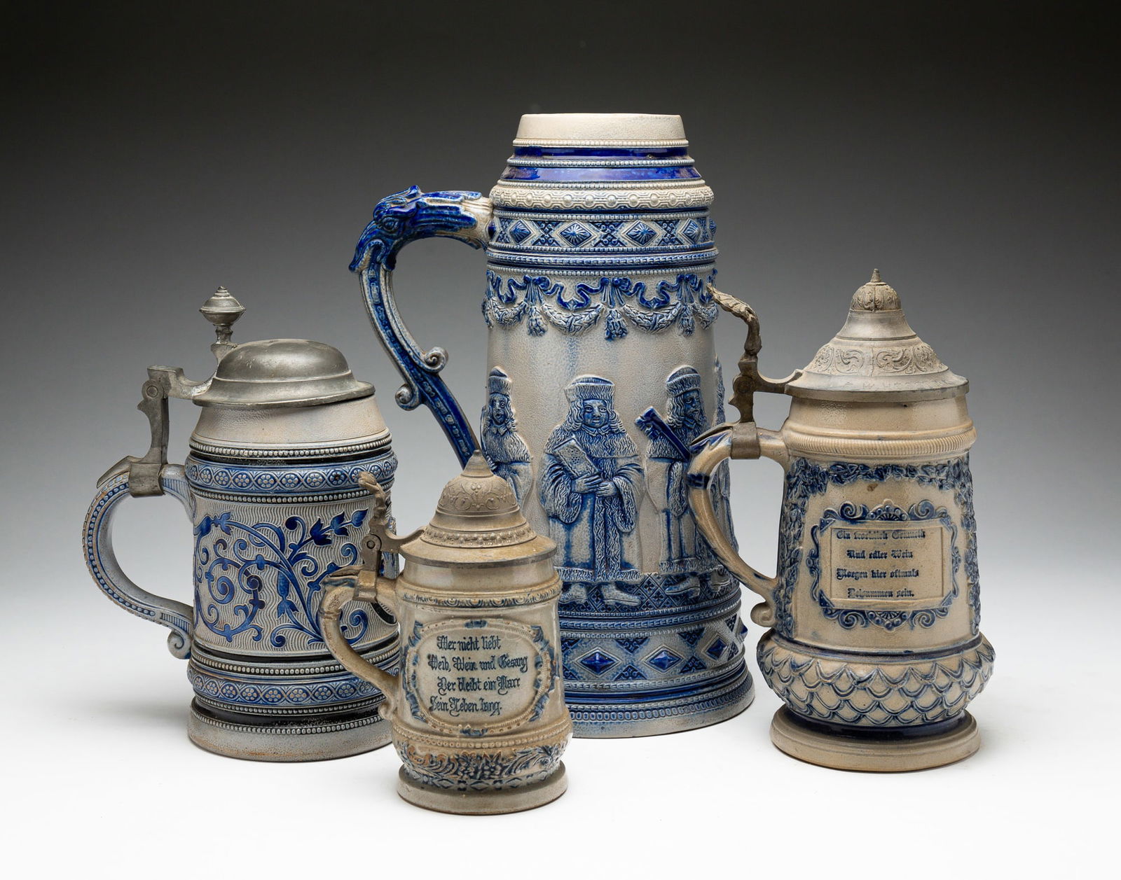 FOUR BLUE AND GRAY SALT-GLAZED STONEWARE STEINS.: American, late-19th to early-20th Century. The first three attributed to Whites Pottery, Utica, NY, the fourth to Reinhold Merkelbach, Höhr, Germany. The first molded with Ecclesiastical figures