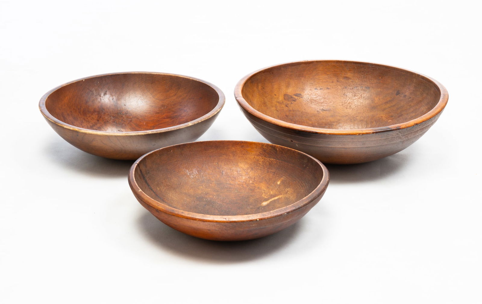 THREE TURNED WOODEN BOWLS.: American, second half 19th Century. Pine. All three have nice wear and patina. The smallest has finely threaded turnings and an age split. 4"h. 12.25"dia. Middle size has been varnished. 4"h. 13.5"dia