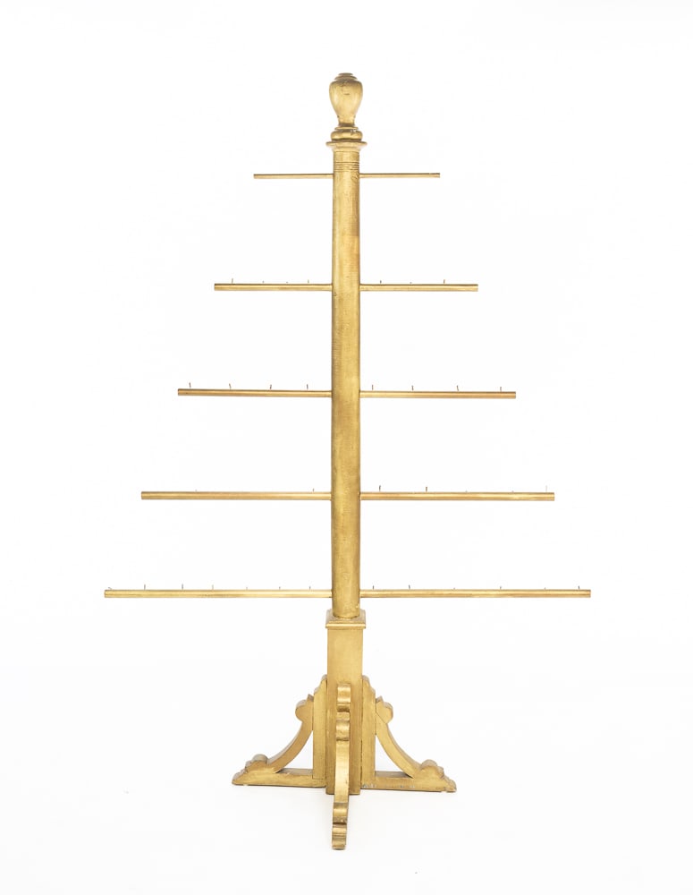 FLOOR DISPLAY RACK.: American, first quarter 20th Century. Mixed woods. Turned post with urn finial, staggered dowel rod arms with "L" hooks, jigsaw cut out bracket base and worn gold repaint. 70"h. 48.5"w.
