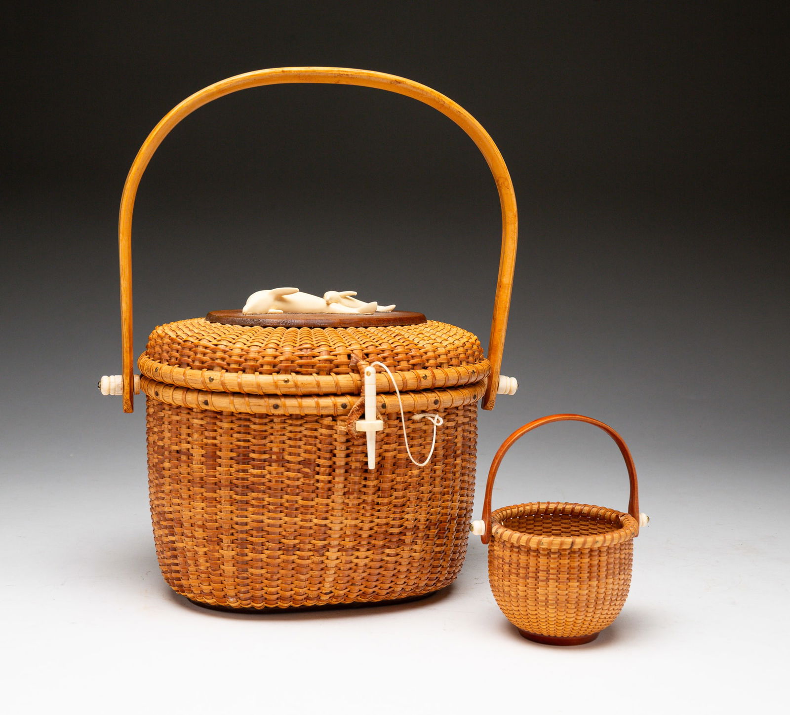 TWO NANTUCKET BASKETS.: American, mid-20th Century. A Barlow basket purse with faux scrimshaw dolphins to the top. Marked to bottom. 7"h. Plus swing handle. Together with a miniature swing handle basket with scrimshaw accent