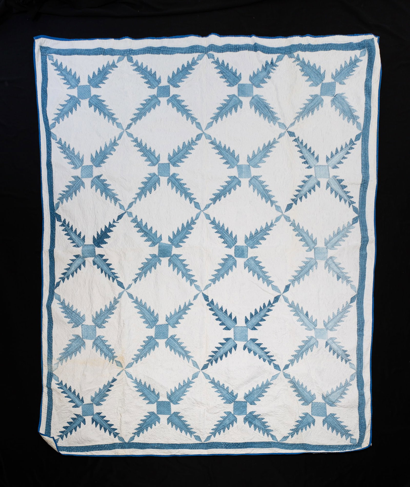 PIECEWORK QUILT IN SNOWFLAKE PATTERN.: American, 20th Century. Blue snowflake pattern on a white ground with a bound blue edge. Staining and a small tear at edge. 76"w. 180"l.