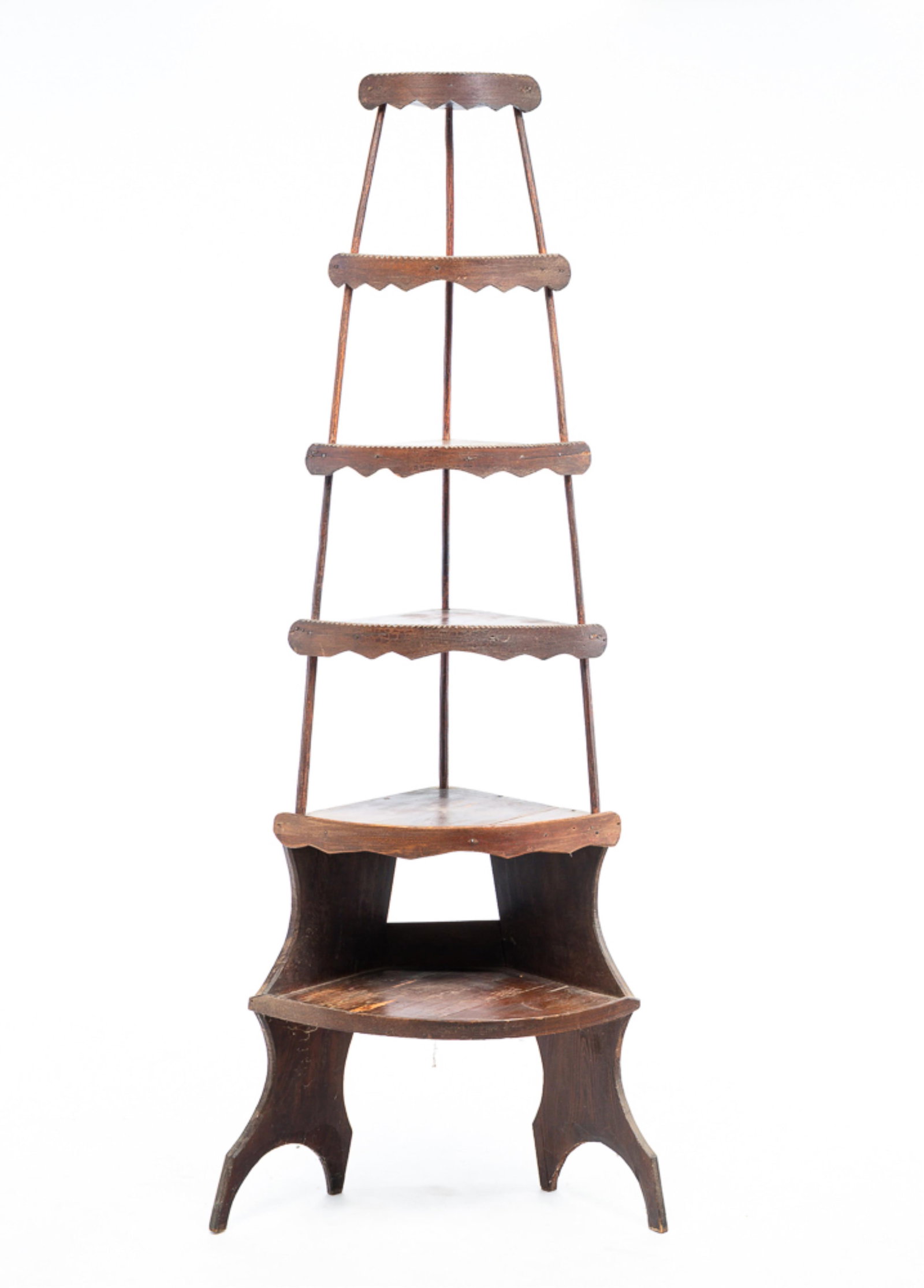 FOLKSY CORNER WHAT-NOT STAND.: American, late-19th Century. Mixed woods. Six graduated quarter round shelves with scalloped and chip carved front gallery edge, small branch supports, base with shaped ends, legs with boot jack cut o