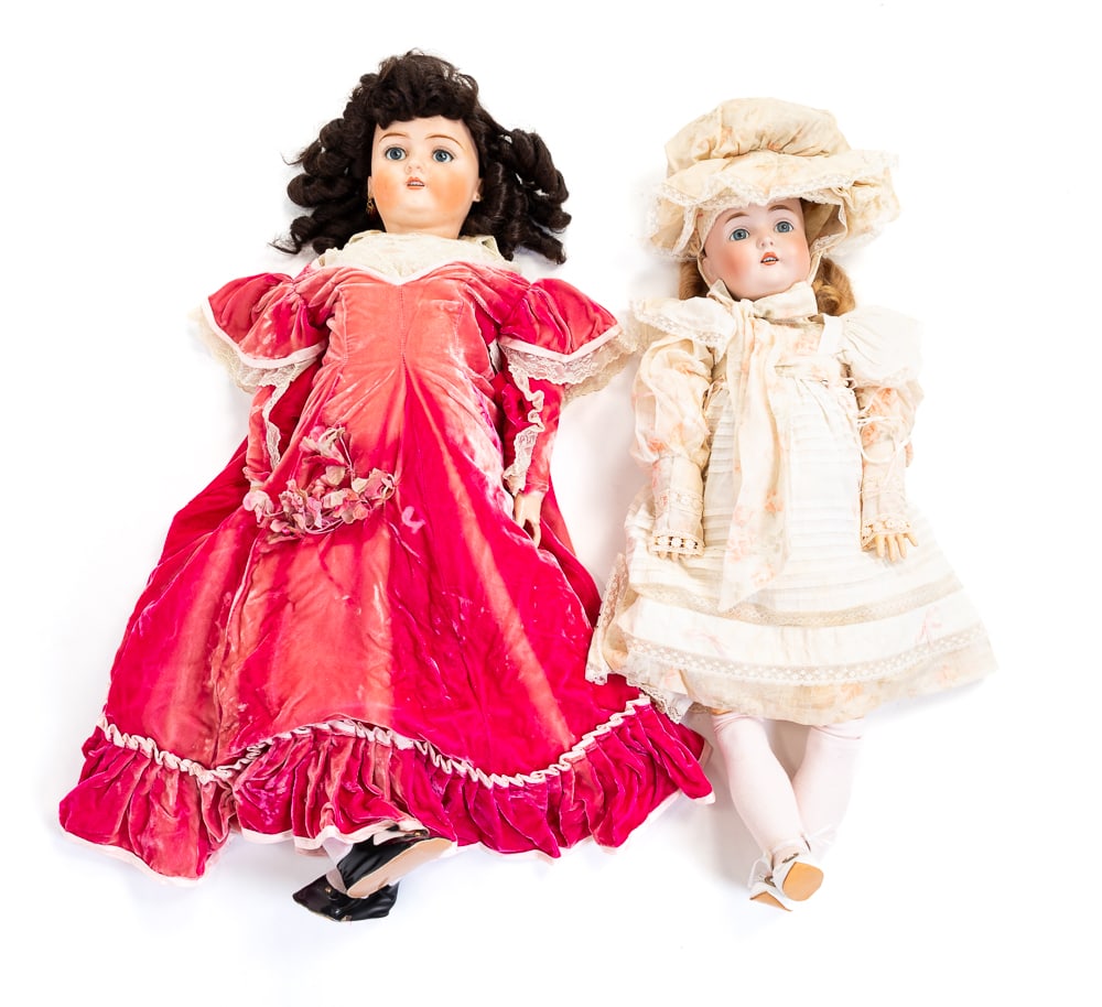 TWO BISQUE HEAD DOLLS.: German, circa 1900. Both have fixed eyes and jointed composition bodies. The doll with black wig is by Bruno Schmidt. Newer clothes, restored body and missing a finger on left hand. 34"h. The other is