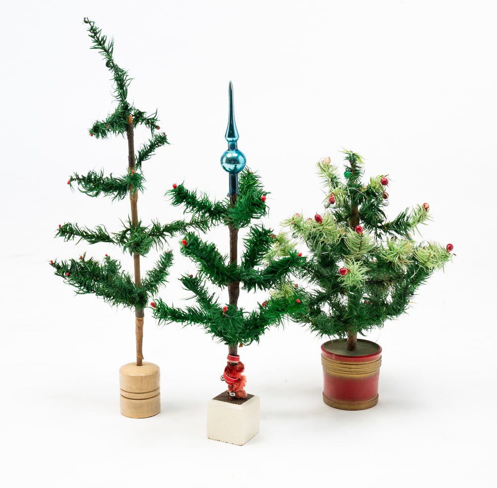 THREE SMALL FEATHER CHRISTMAS TREES.: German, fourth quarter 19th and early-20th Centuries. Green feather trees with tissue paper wrapped trunks. Two with red berry accents and set into wooden painted beige bases, one square and one round