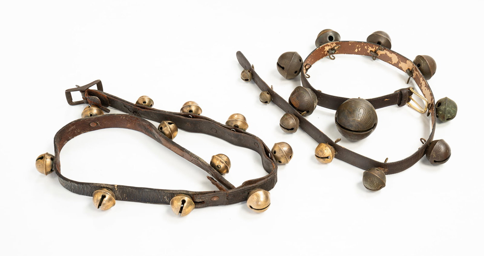 TWO STRAPS OF SLEIGH BELLS.: 19th and 20th Centuries. The first of graduated sized shank-style bells attached to a modern leather belt with bell pins. With wear and oxidation to bells. Cracking and losses to back of belt. 43"l. T