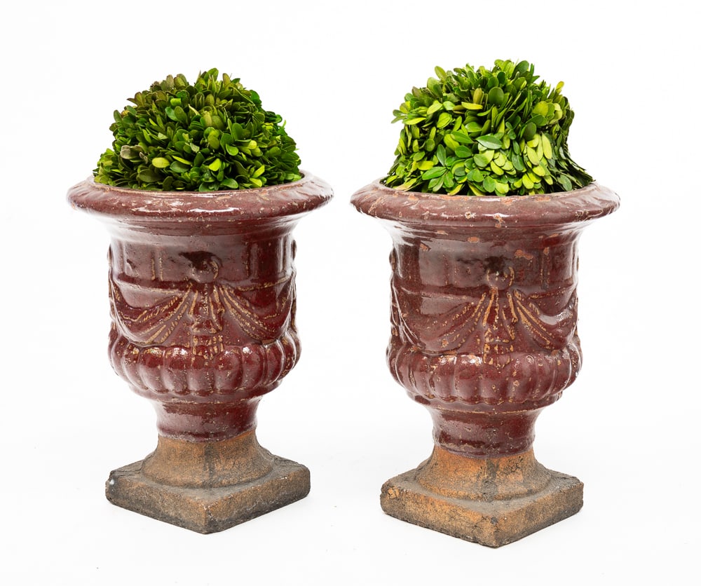PAIR OF GLAZED TERRACOTTA URNS.: European, 20th Century. Red glazed terracotta footed urns with swag accents. Square unglazed bases. Edge wear, glaze loss and finish wear. 11.5"h.