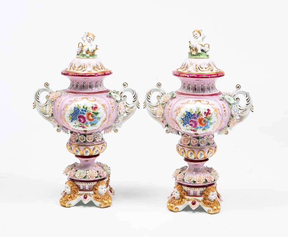 LARGE PAIR OF LIDDED URNS.: Chinese, late-20th Century. Porcelain. Pink bodies, gold trim, putti finials on lids. Painted and applied floral decoration. Leaf bracket open handles and bases with putti heads above scrolled feet. F