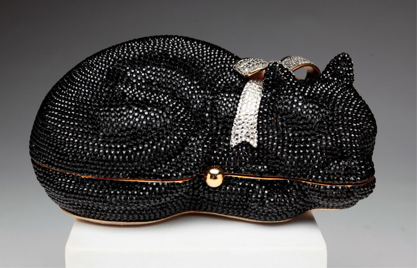 JUDITH LEIBER SLEEPING CAT MINAUDIERE.: American, early-21st century. Judith Leiber sleeping cat form clutch. Black jeweled exterior on a gold-tone frame, with rhinestone bow collar, pressure clasp closure. The clutch is lined with gold lea