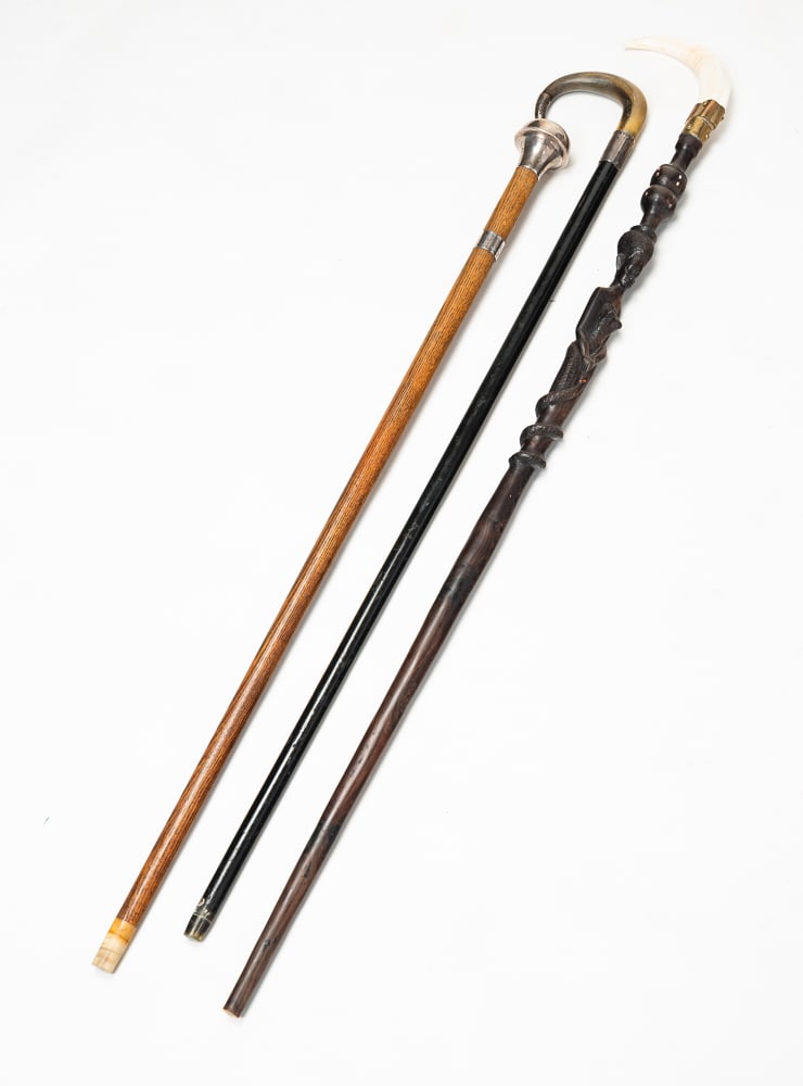 THREE CANES.: Late-19th and early-20th Centuries. An African carved ebony with female figure and snake with boar's tusk handle. 40"l. An English cane with horn handle, sterling band and cap. 36"l. And American oak 