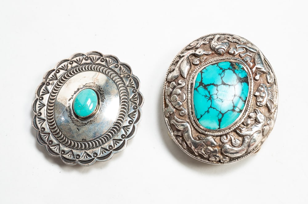 TWO SILVER BELT BUCKLES.: Mid- to late-20th Century. Oval shape with raised silverwork decoration of flora and fauna surrounding a large Kingman turquoise stone, the back with raised silverwork decoration of a bird amid scroll