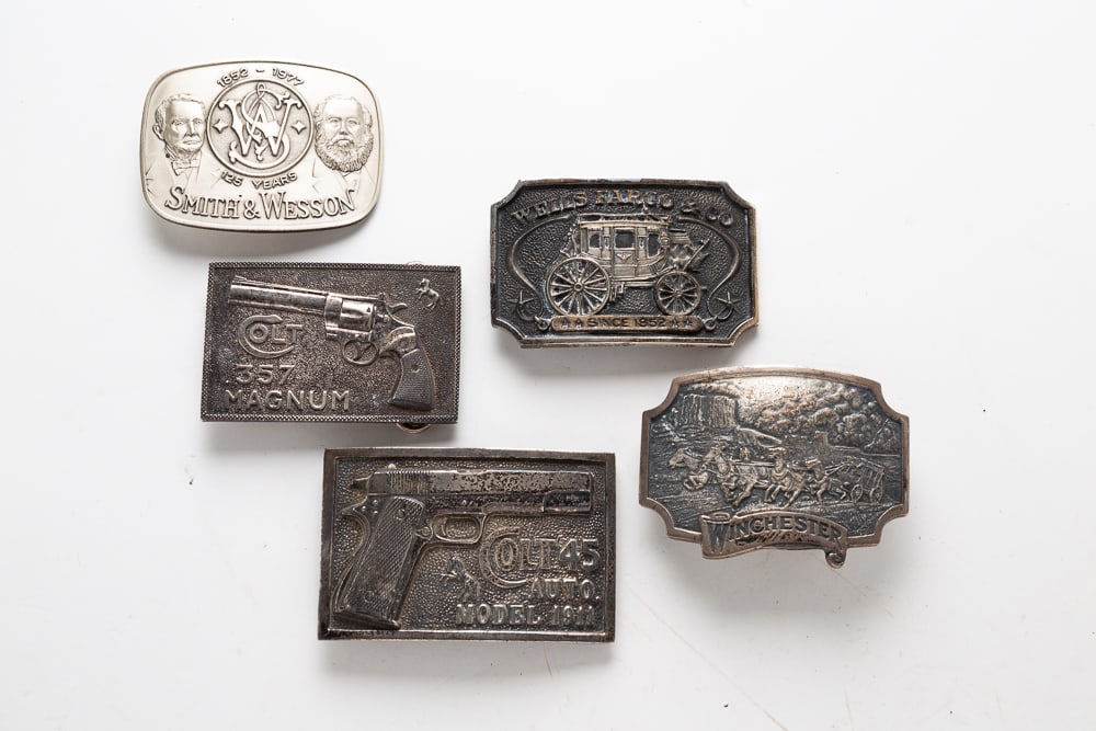 FIVE STERLING SILVER BELT BUCKLES.: American, 1970s. Smith & Wesson 125 Years commemorative belt buckle in case. Stamped "1977 SMITH & WESSON SERIAL NUMBER 0128 STERLING" on back. 3.25"w. Winchester belt buckle in case. Stamped "WINCHES