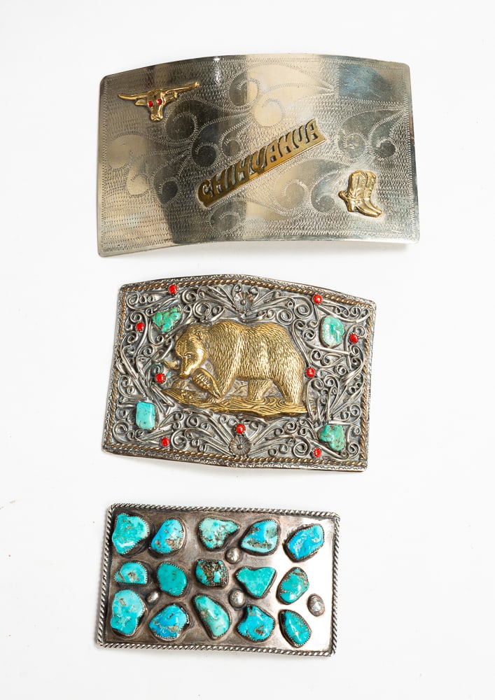 THREE LARGE SILVER BELT BUCKLES.: Mid- to late-20th Century. Rectangular shape with 15 sawtooth bezel-set Kingman turquoises. Unmarked. 3"h. 5"w. Rectangular shape with golden bear eating a fish amid scrolling silverwork and flowers w