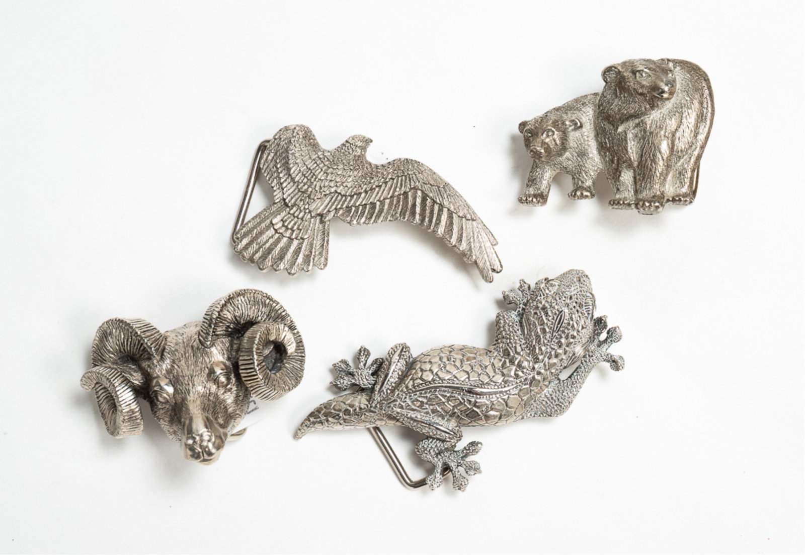 FOUR WATHNE SILVER BELT BUCKLES.: American, second half 20th Century. Ram's head. Stamped with crown hallmark and "WATHNE LTD." on back. 2.75"w. Two bears. Stamped with crown hallmark and "WATHNE LTD." on back. 3.25"w. Eagle with one 