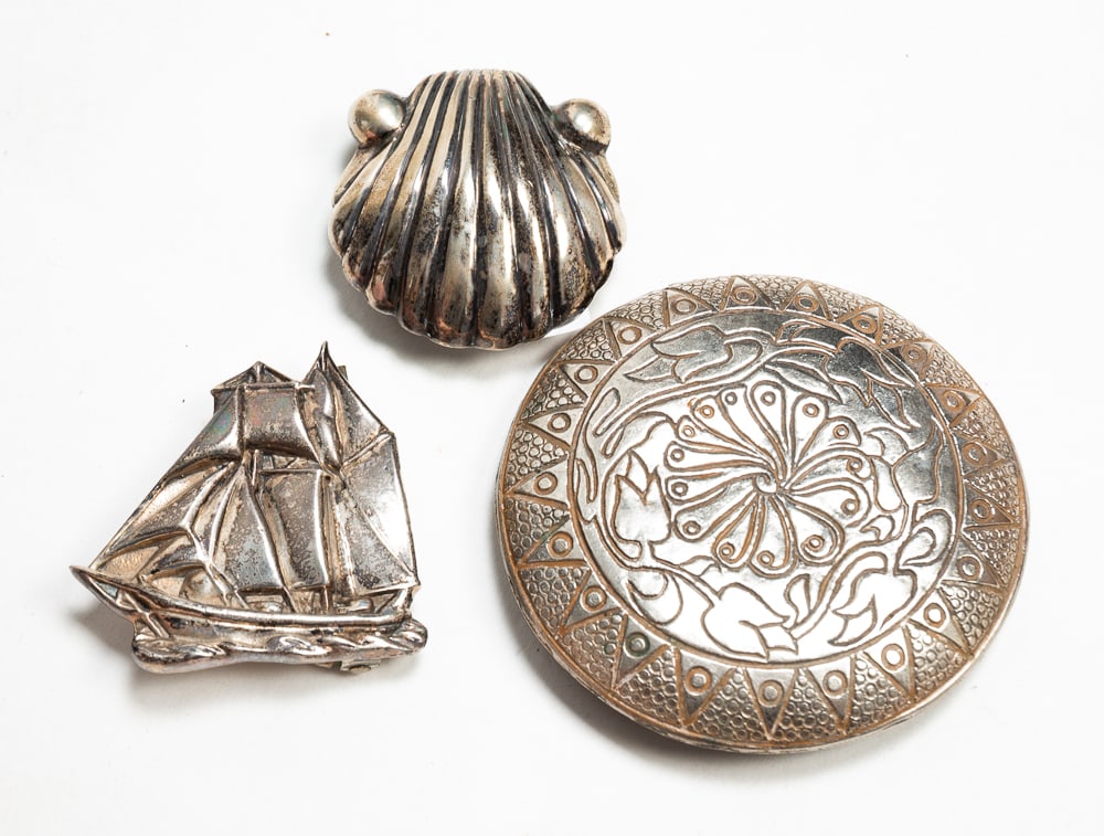 THREE SILVER BELT BUCKLES.: Mid- to late-20th Century. Shell and bead design. Marked "925" on back. 2"w. Circular shape with floral and feather design. Unmarked. 3.5"dia. Sailboat design. Unmarked. 2.25"w. Total weight of all ap