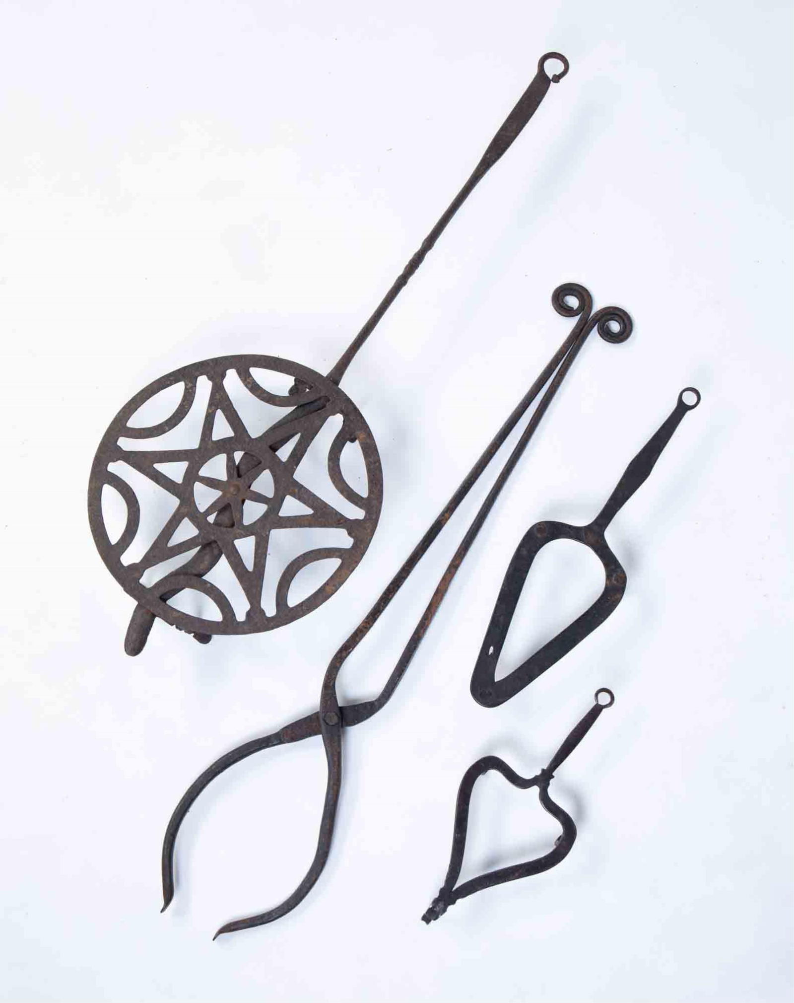 FOUR PIECES OF FORGED IRON.: American, 19th Century. Broiler with star decoration and snake head. 24.5"l. Tongs with ram's head handles. 24"l. Ovoid trivet with riveted legs. 12.25"l. Heart for trivet with notched end. 9"l.
