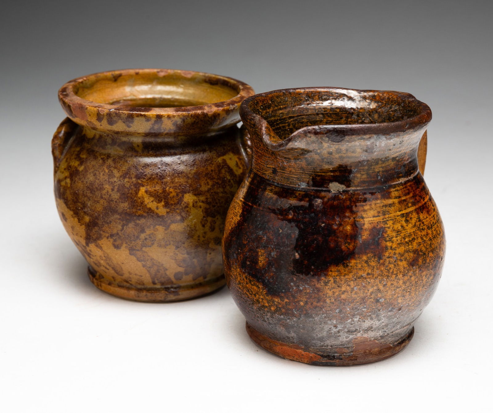 REDWARE SUGAR AND CREAM PITCHER.: REDWARE SUGAR AND CREAM PITCHER. American, 19th Century. Cream pitcher in yellow and black mottled glaze with handle. 4.5"h. Sugar in yellow and black mottled glaze with two lug handles. No lid. 4"h.