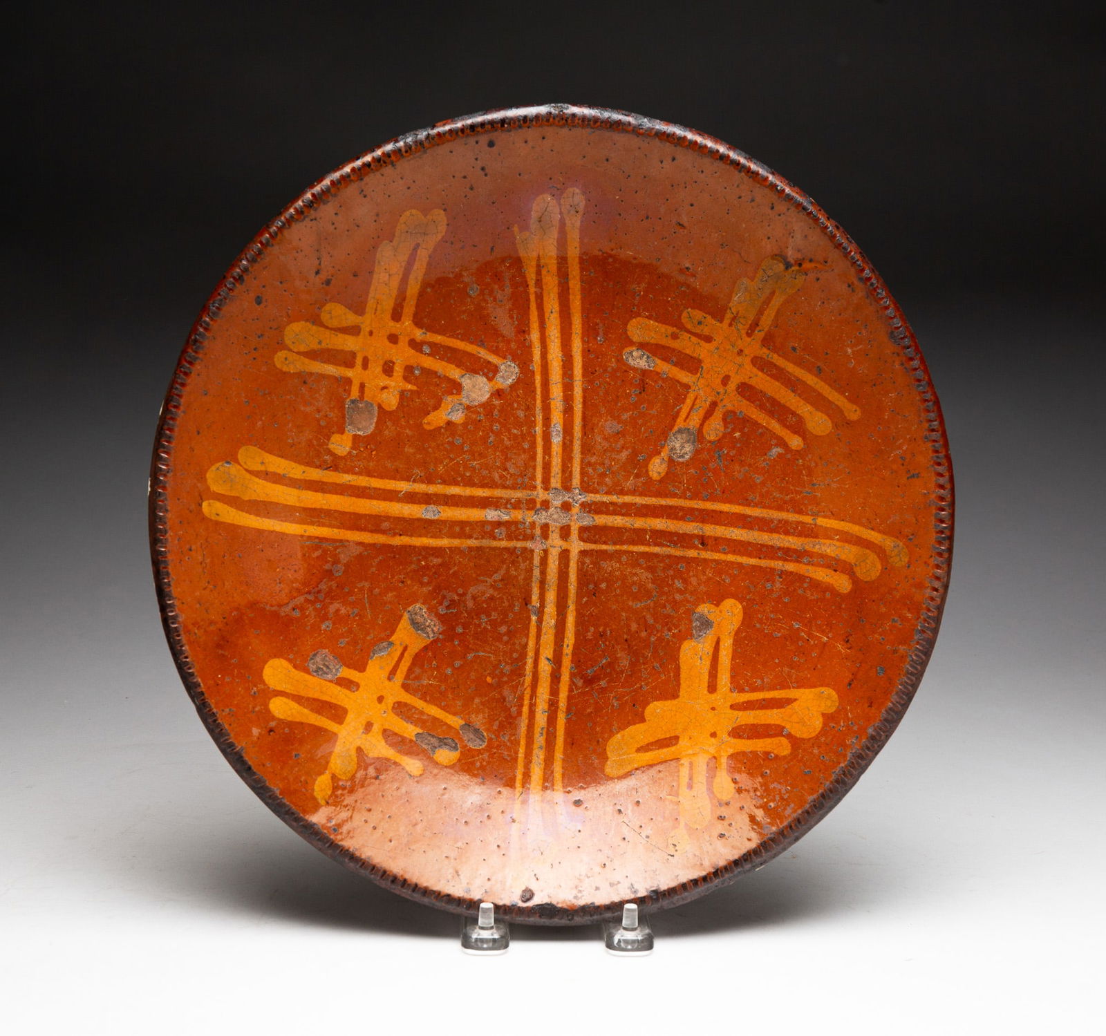 SLIP DECORATED REDWARE PLATE.: SLIP DECORATED REDWARE PLATE. American (Pennsylvania), 19th Century. Orange glaze with yellow "X" decoration and coggled rim. 2"h. 12.5"d. From the collection of Carol Schulman (Chesterland, Ohio).