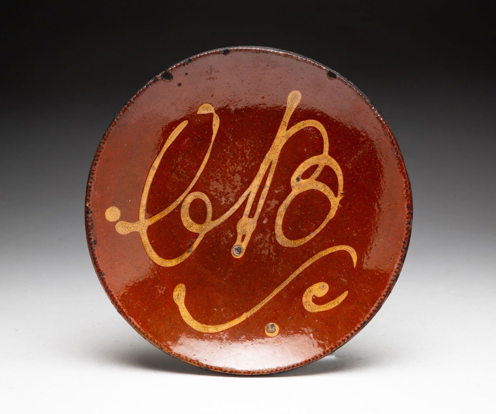 SLIP DECORATED REDWARE PLATE.: SLIP DECORATED REDWARE PLATE. American (Pennsylvania), 19th Century. Orange glaze decorated with yellow squiggly lines, possibly the initials "CB," with coggled rim. 1.5"h. 9"d. Sold at Garth's Auctio