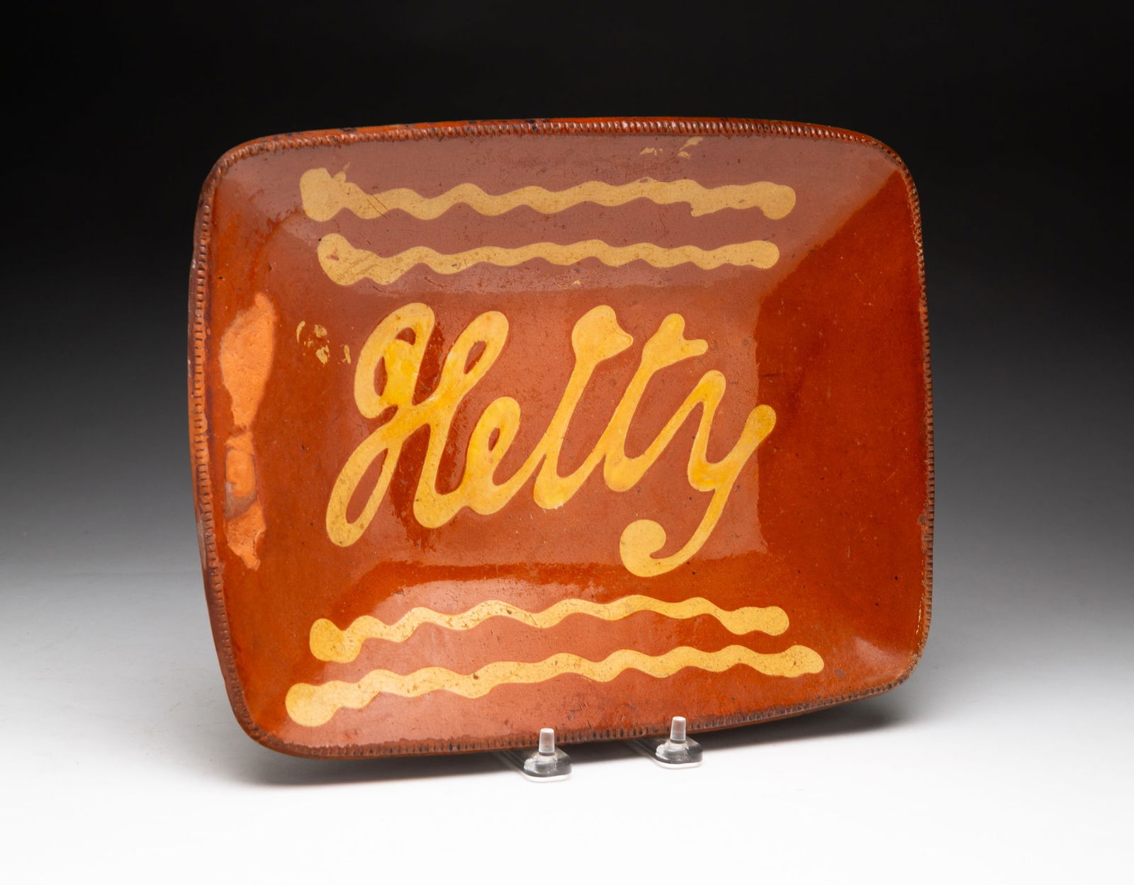 "HETTY" REDWARE LOAF DISH.: "HETTY" REDWARE LOAF DISH. American, 19th Century. Scarce shape with yellow slip decoration. 2"h. 12"w. 9.5"d. Ex Lewis Scranton (Killingworth, Connecticut). From the collection of Carol Schulman (Che